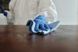 person in white cleaning suit with blue gloves on wipes wooden side